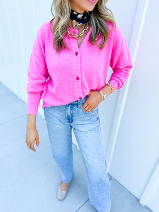Person wearing a bright pink cardigan and light blue jeans against a white background