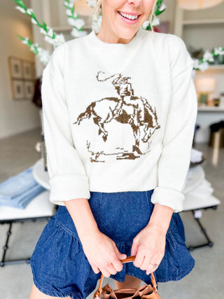 Person wearing a white sweatshirt with a graphic design of a person on a horse, standing in an indoor setting.