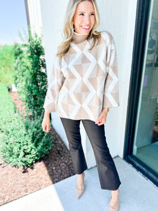 Woman wearing a beige and white patterned sweater and black pants standing outdoors.