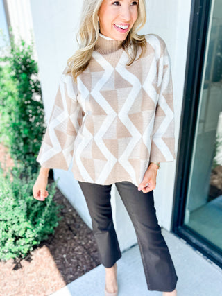 Woman wearing a beige and white patterned sweater with black pants outdoors.
