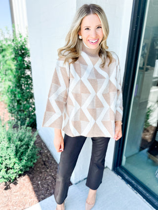 Woman wearing a beige and white patterned sweater with black pants standing outside.