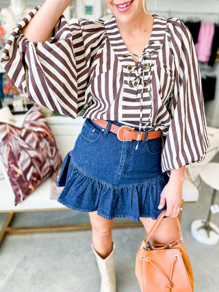 Woman wearing a striped blouse and denim skirt with a brown belt, holding an orange handbag.