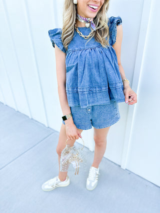 Girl standing in front of a white wall, wearing a denim top and denim short set.