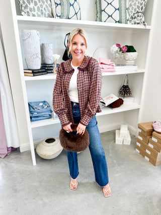 Woman holding a brown fur item in front of a white bookshelf filled with decorative items.
