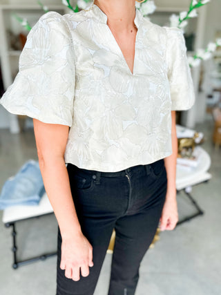 Person wearing a white blouse with ruffled sleeves and black pants in an indoor setting.