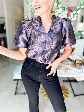 Woman wearing a purple floral blouse and black pants in an indoor setting.
