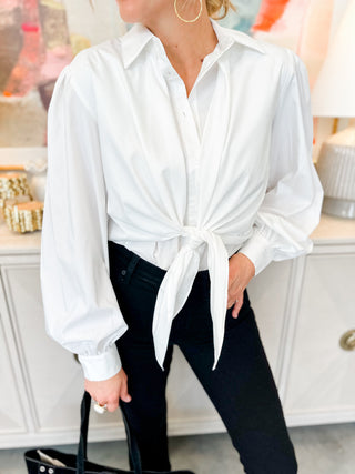 Person wearing a white tied blouse with black pants in an indoor setting