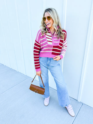 Woman wearing a striped sweater and jeans, holding a brown bag against a white background